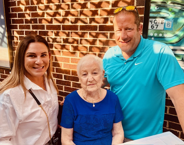 Three people stand close together and pose inside a restaurant with brick walls, framed artwork, and a mural in the background.